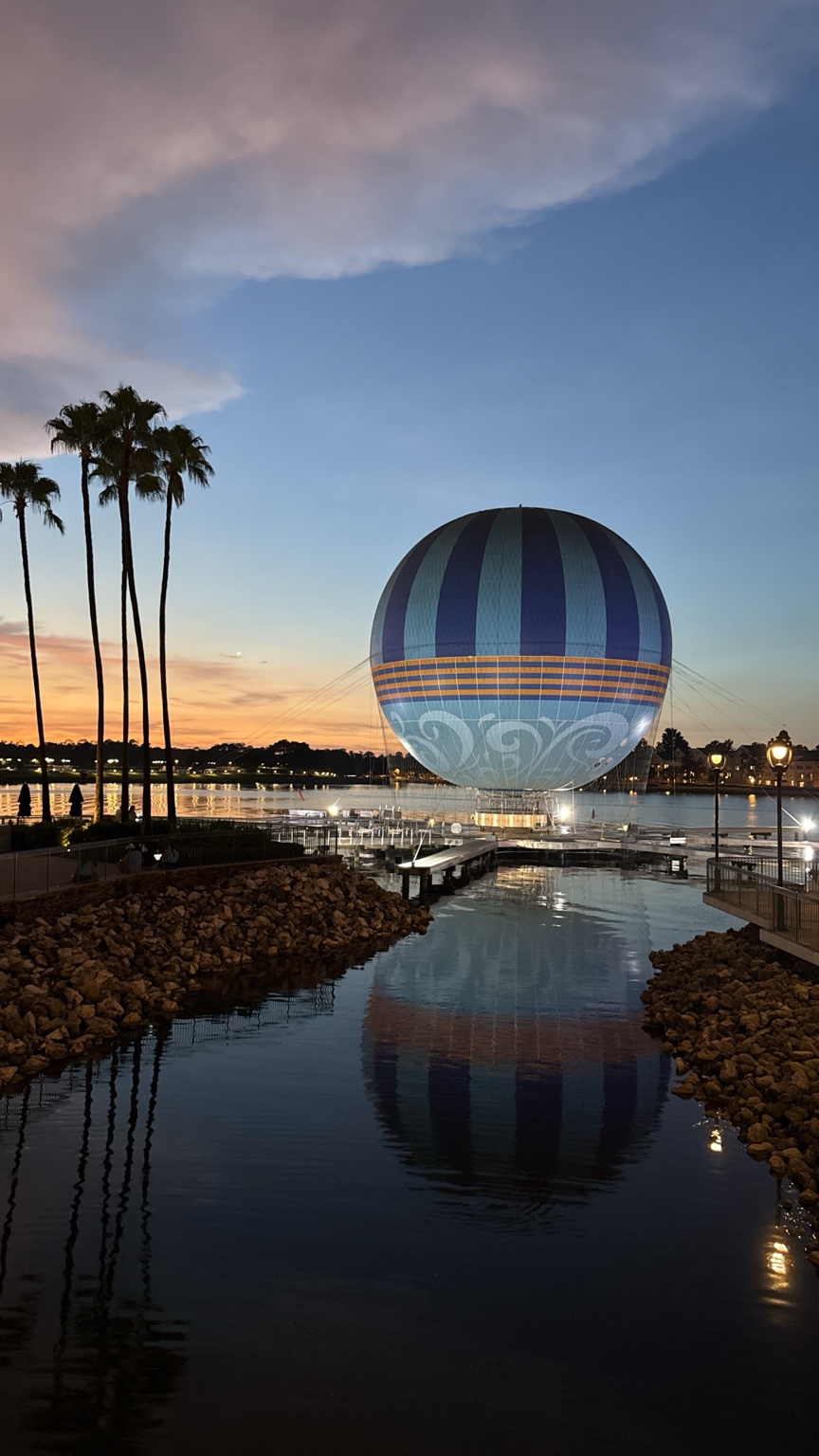 Globo de Disney Springs al atardecer, con palmeras y su reflejo en el agua