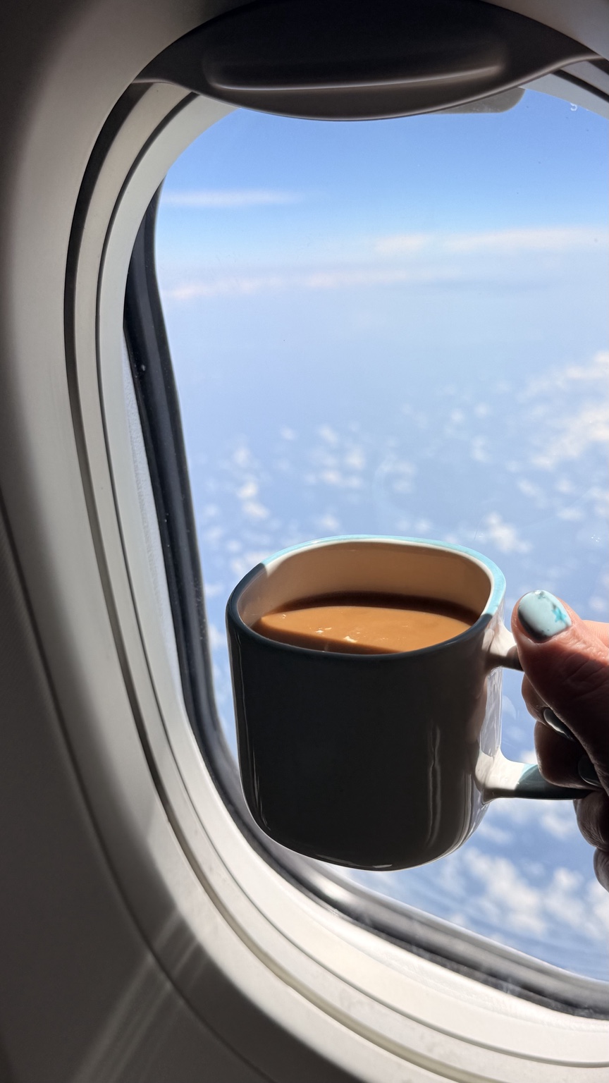 Una taza de café junto a la ventanilla de un avión, con el cielo al fondo